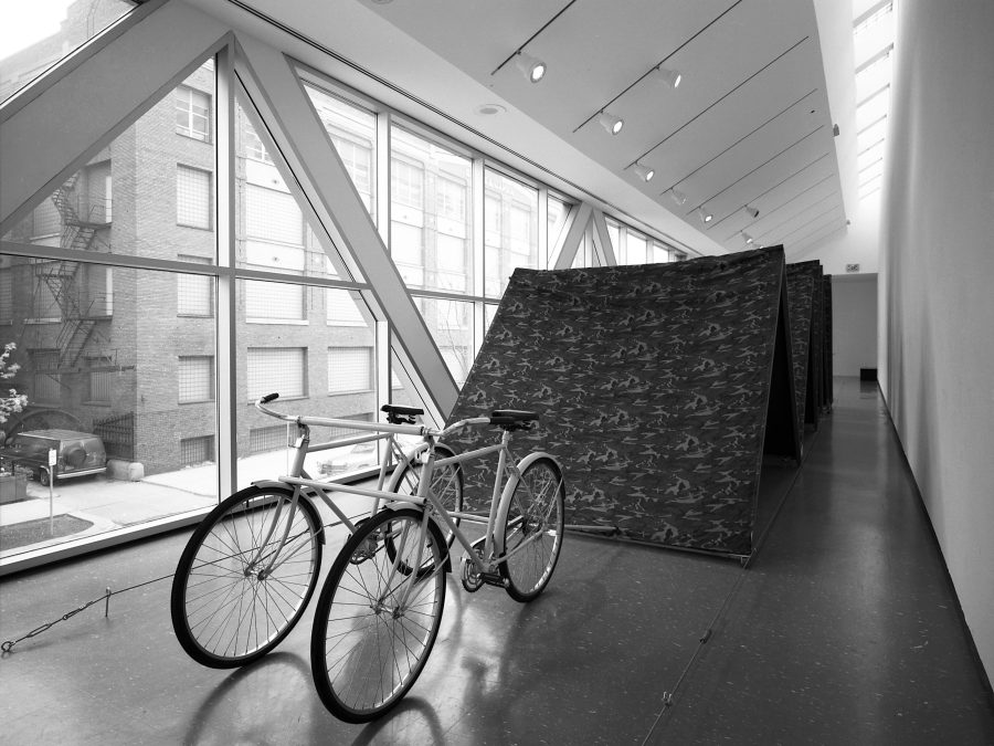 Two bikes attached to large fabric boards in a hallway with windows filling one side