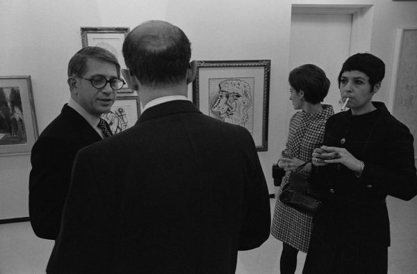 Black-and-white photograph of four people in 70s clothing discussing art in a gallery