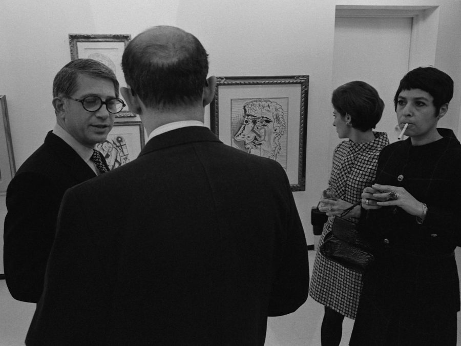 Black-and-white photograph of four people in 70s clothing discussing art in a gallery