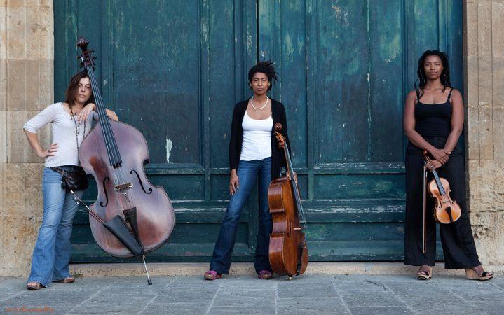 Photo of three women with stringed instruments in front of a building