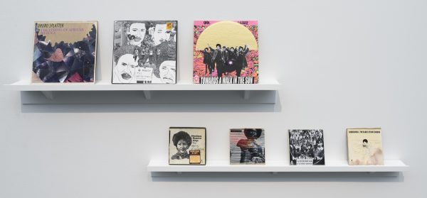 Two wall shelves display a group of illustrated album covers