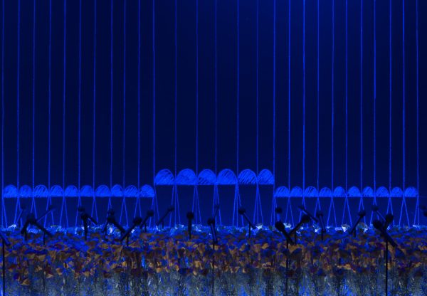 Mixed media installation with microphones planted among flowers and a geometric chalk drawing in the background, bathed in a rich blue light