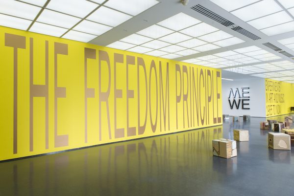 The bright yellow entry wall of an exhibition bears the floor-to-ceiling title, 