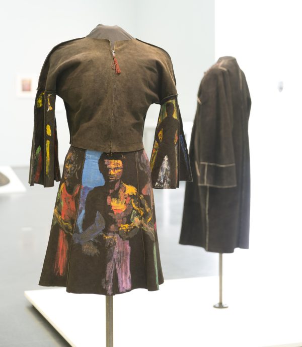 A suede dress features hand-painted figures in bright colors on its skirt and flared sleeves