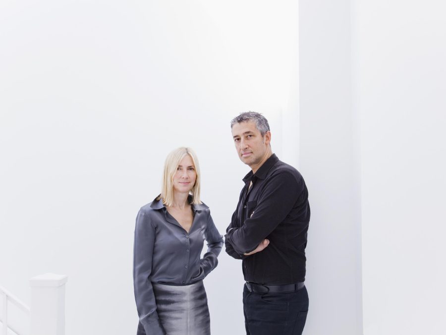 A woman and man in business casual clothing pose in front of a white wall