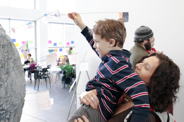 A woman lifts a young boy to help him plant a handmade flag in a large-scale model of a planet.