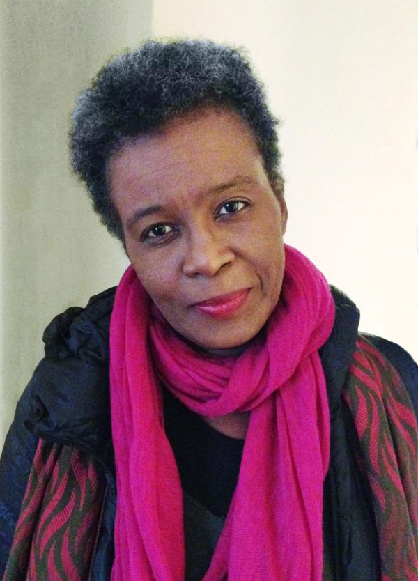A photographic portrait shows a middle-aged, dark-skinned woman cocking her head and wearing a bright pink scarf.