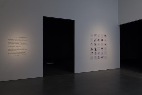 A four-by-six grid of square drawings on a wall between two large black doorways