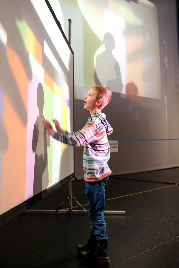 A young boy reaches out to touch a screen projected with a grid of colorful rectangles.