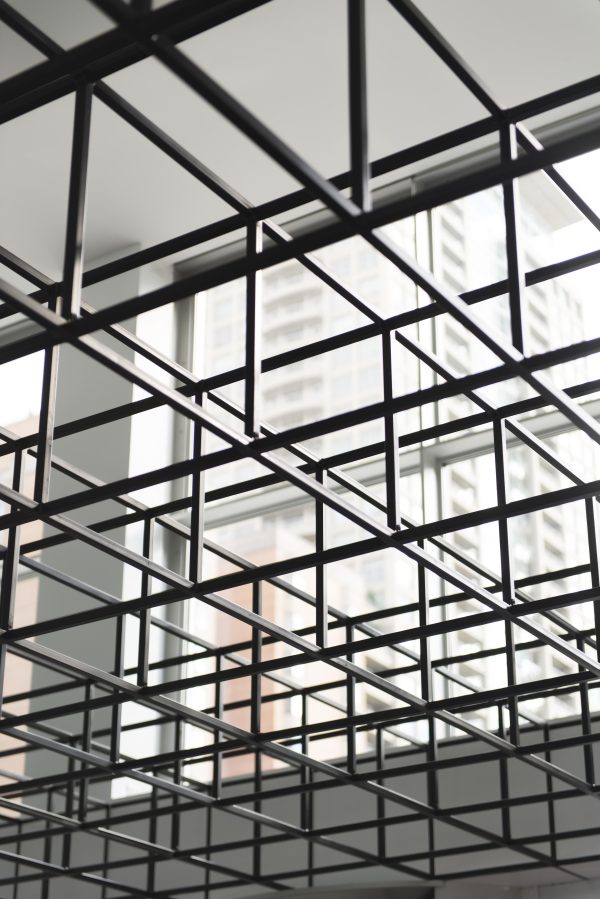 A grid of black, open-sided cubes photographed from below with a large window in the background