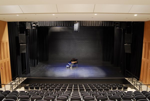 A grand piano on a stage viewed from the back of an empty theater