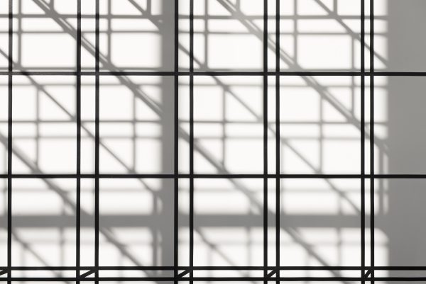 Black lines form illusionistic cubes on a wall cast with geometric shadows.