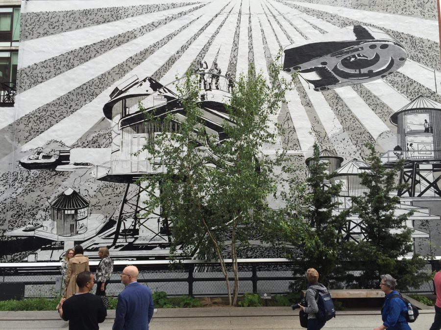 People in a park pass by a large black-and-white mural whose illustrations blend classic urban structures with sci-fi elements.