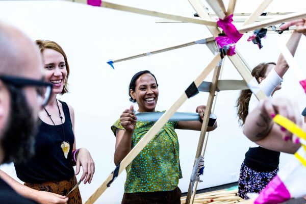 A group of people next to a structure put together with pink and black duct tape. One person starts to rip a new piece of duct tape off the roll.