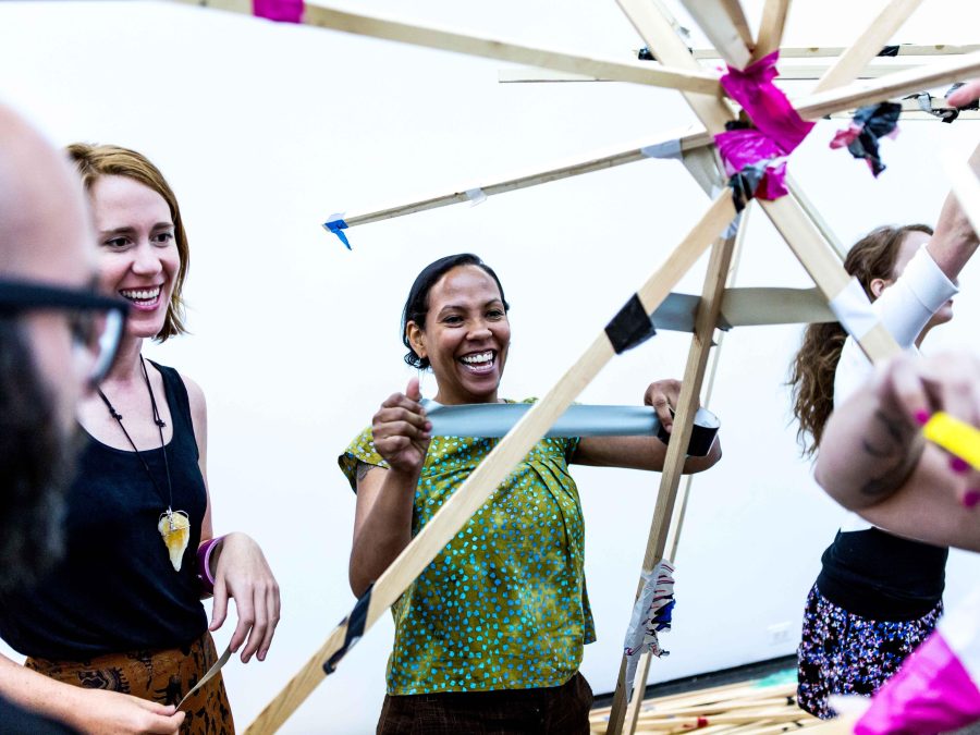 A group of people next to a structure put together with pink and black duct tape. One person starts to rip a new piece of duct tape off the roll.