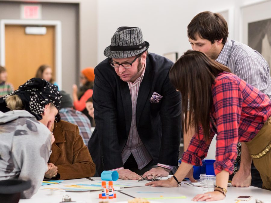 People in discussion lean over a table covered with papers.