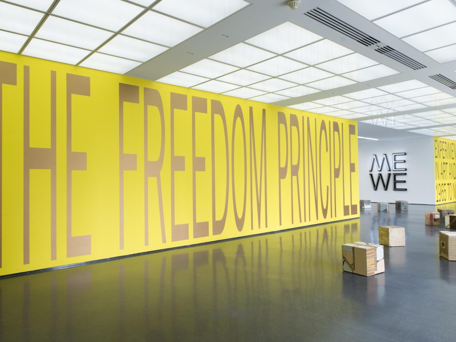 The bright yellow entry wall of an exhibition bears the floor-to-ceiling title, 