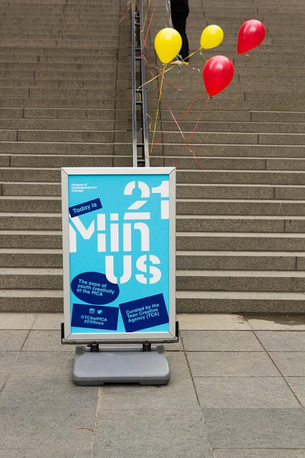 A windboard displaying a blue poster for 21Minus with red and yellow balloons attached to it in front of a set of long grey steps