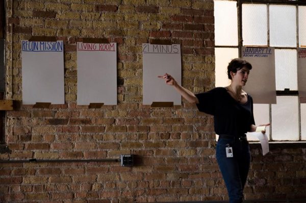 Lyra Hill speaks in front of a series of posters hung along a brick wall. The signs read: 