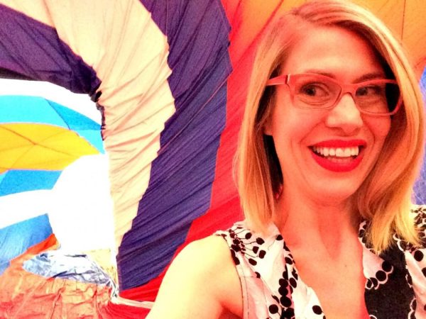 A blond woman with red glasses takes a selfie in a room covered in a red white and blue fabric