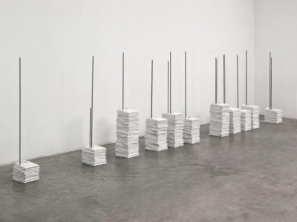 Stacks of folded white polo shirts are pierced by vertical metal rods.