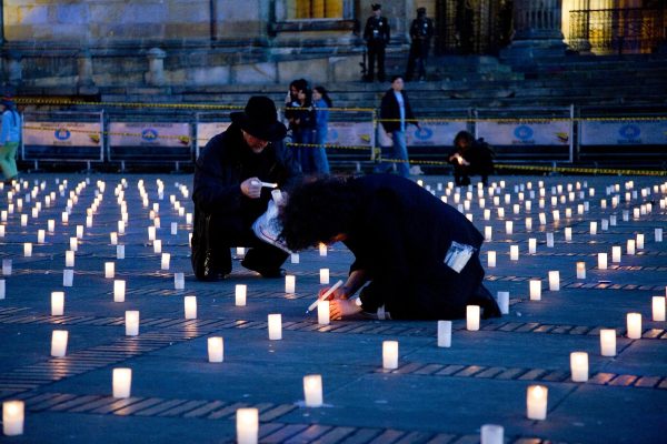 Two people sit and light candles among rows and rows of candles