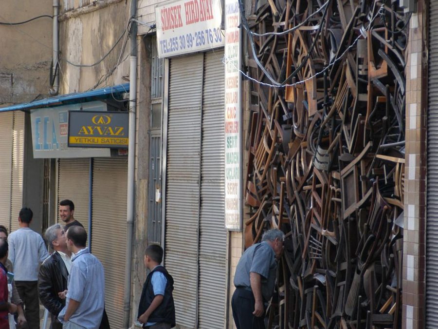 A man bends forward for a closer look at hundreds of stacked wooden chairs filling an alley.