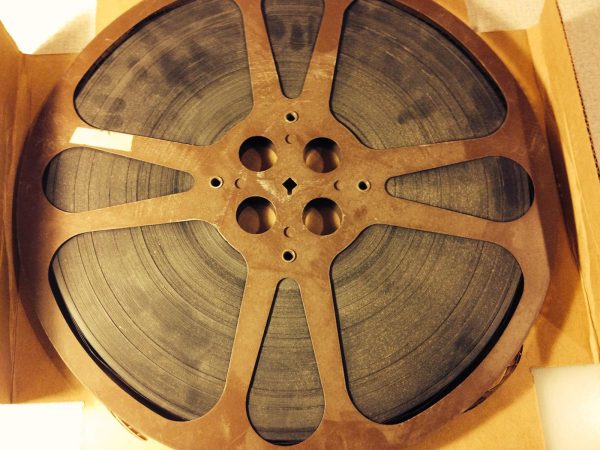A rusty 16mm metal reel full of film sits in an open cardboard box.