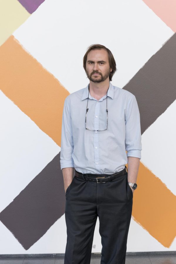 Former MCA curator Dieter Roelstraete stands in front of a wall painted with multicolor exes.