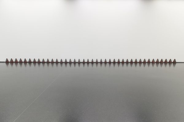 A row of thirty-nine small red and black cones lined up against a white wall