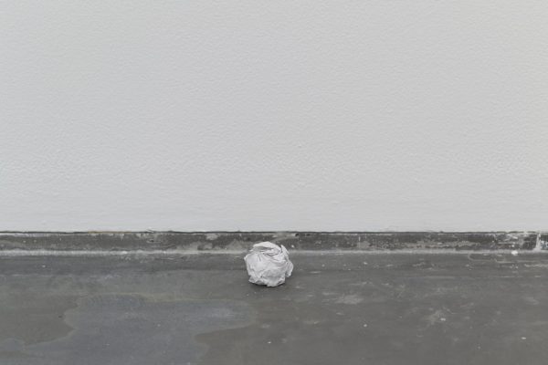 A white crumpled ball of paper on a grey floor near a white wall