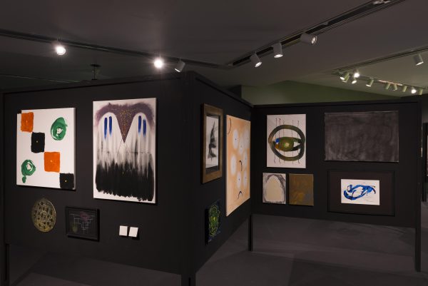 Colorful, abstract paintings hung in clusters on a black folding display board