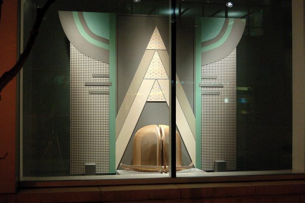 An art deco window display featuring greys and teals highlighting a larger than life bowler hat