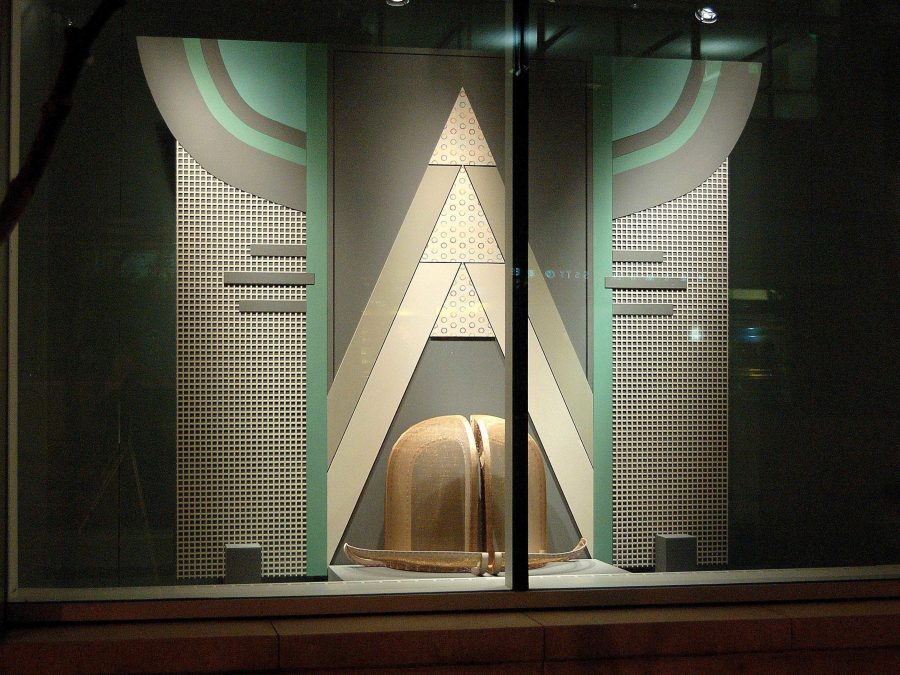 An art deco window display featuring greys and teals highlighting a larger than life bowler hat