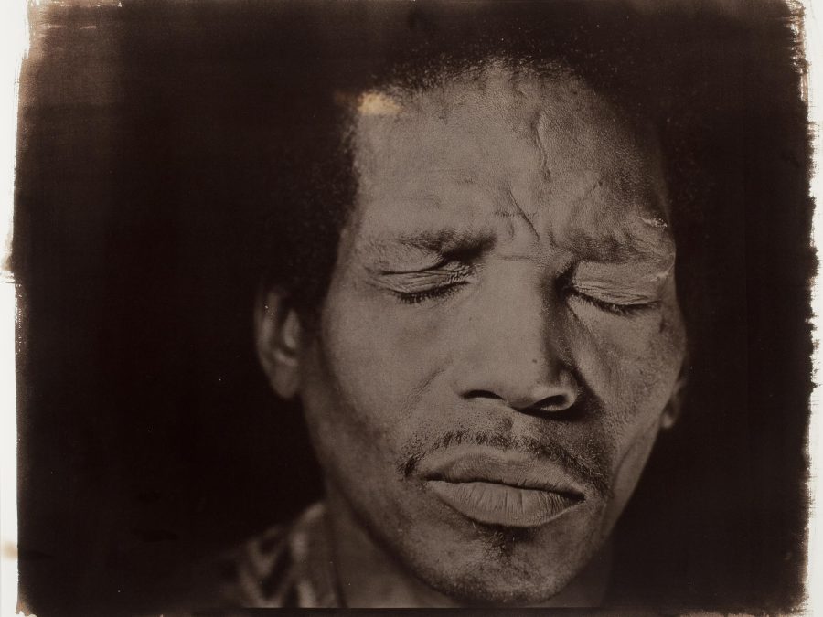 A brown-toned photograph featuring a close-up of a male-presenting person with their eyes closed