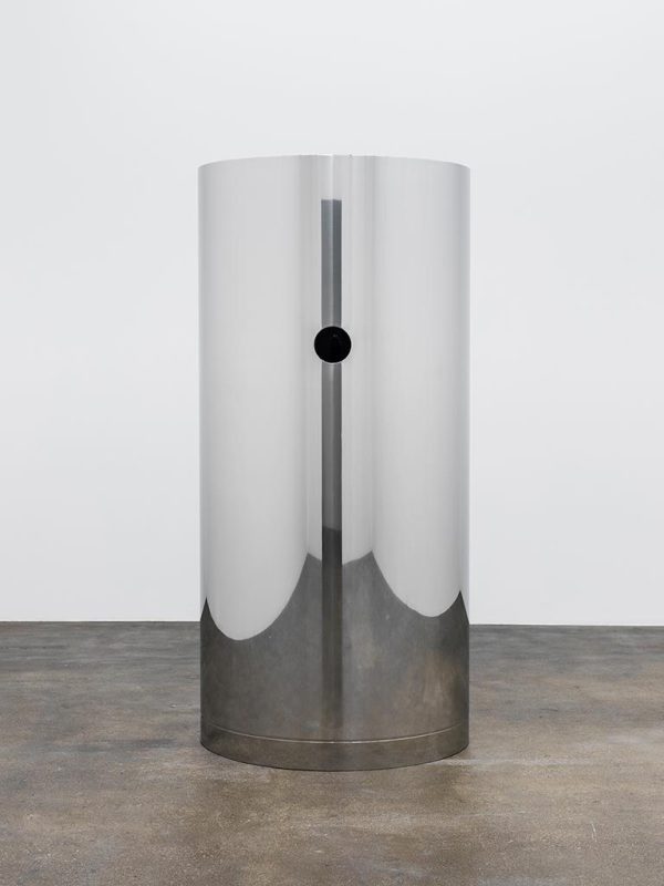 A steel cylinder with a hole at average adult eye height in a white gallery space