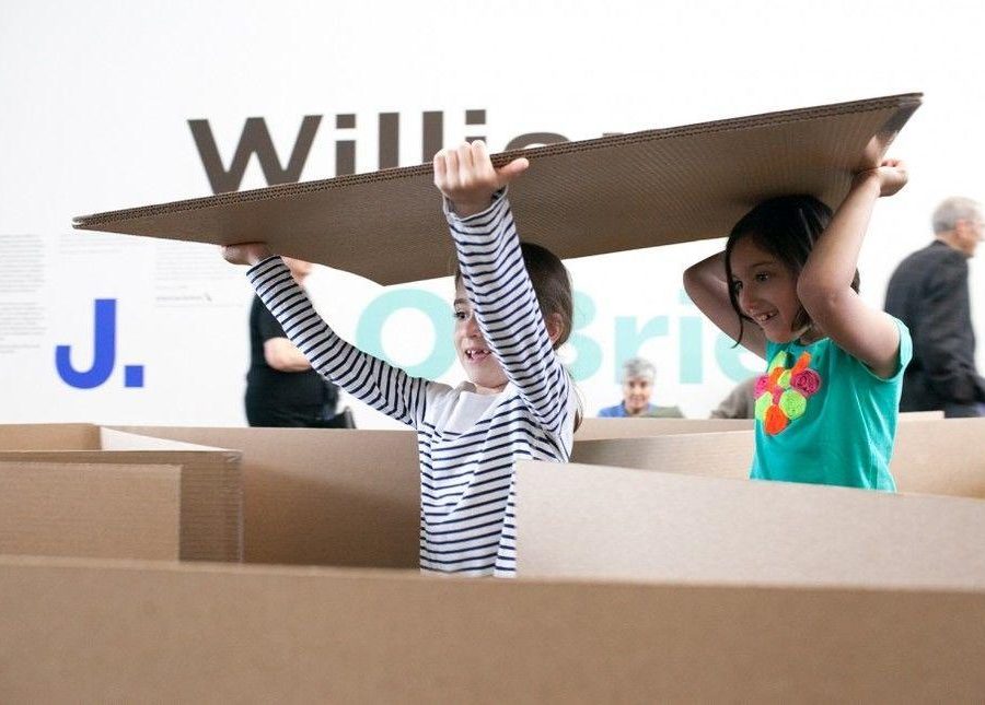 Two children carrying a cardboard sheet through a cardboard maze
