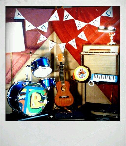 Polaroid of a pile of band gear in front of red curtains partially open to display brown boxes