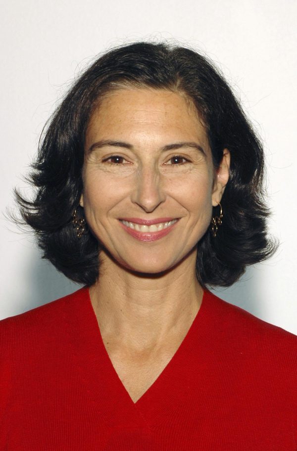 A middle-aged woman with dark shoulder-length hair wearing a red v-neck sweater smiles.