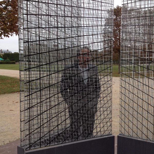 A person stands behind a series of grids that obscure their figure in a park pathway