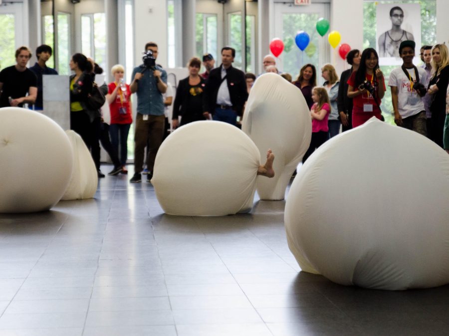 Feet stick out of four large white balls as a crowd looks on