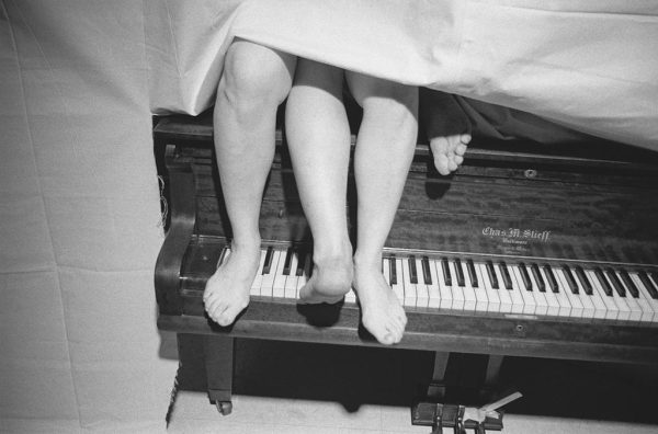 Two pairs of feet appear from under a piece of fabric on a grand piano's keys
