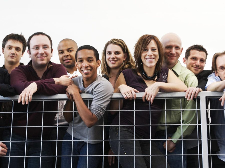 Sixteen members from the International Contemporary Ensemble lean over a metal guard rail.