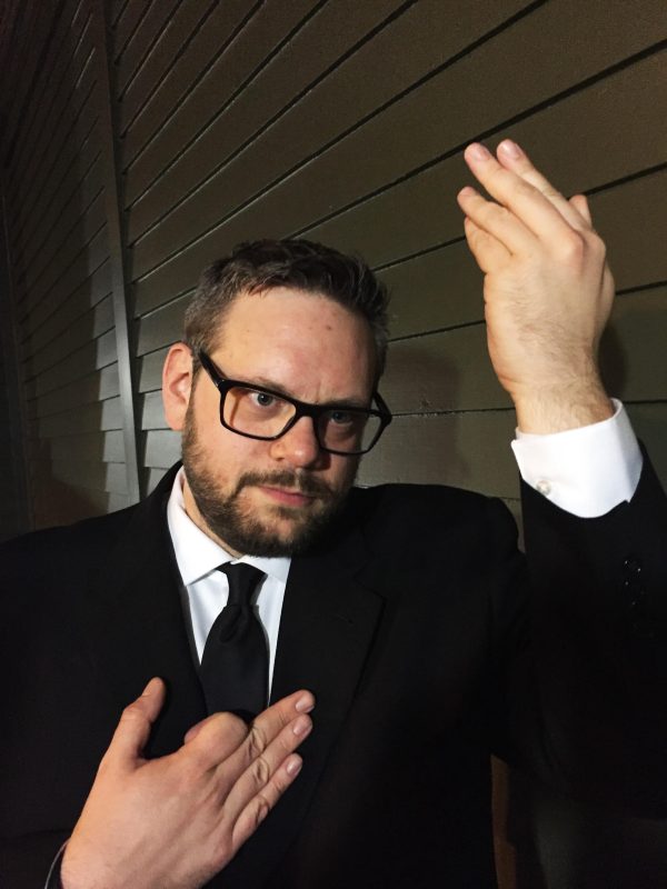 A light-skinned male with dark glasses, short brown hair, and a beard poses like David Bowie on the cover of the changes album with right hand angled up and his left hand on his heart