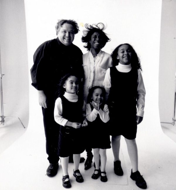 Black and white family portrait of two adults and three children standing within a visible white portrait screen