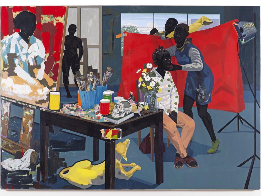 A black woman poses in a chair against a vivid red backdrop while a woman adjusts her head and a man gets dressed behind the backdrop. The painted portrait in progress is shown on an easel at left, next to a table strewn with paints and paintbrushes, a skull, and vase with flowers. A yellow dog rests on the floor below the table. A nude figure stands in the background.