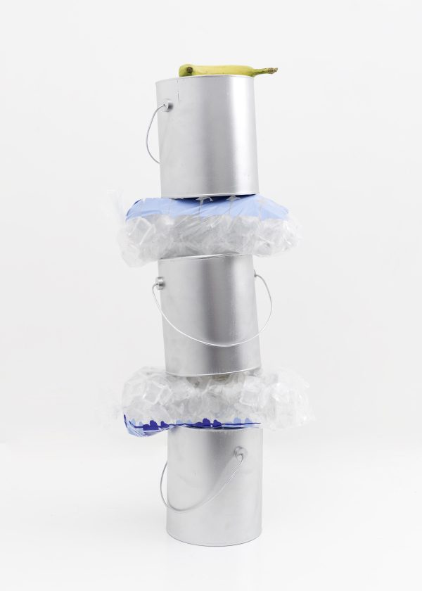 A yellow banana rests on top of a column made up of three silver paint cans and two bags of ice. The bags of ice are sandwiched in between the paint cans.
