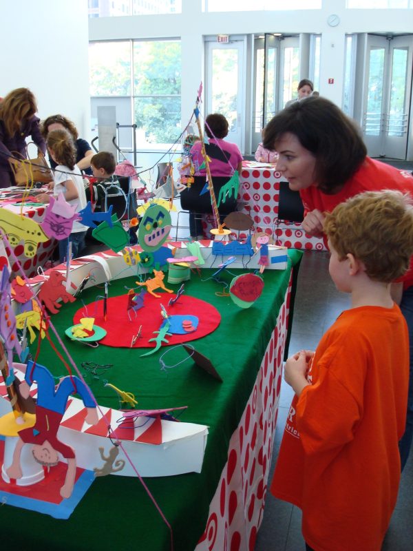 A woman and young boy look at a colorful display in the museum's lobby of paper and felt cut-outs that fill a table and resemble a circus with animals and acrobats.