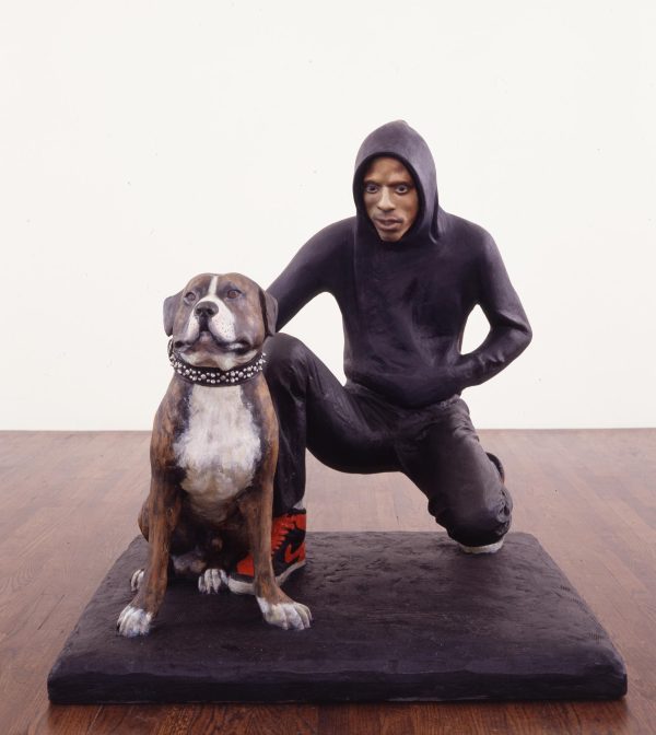 Sculpture of a dark-skinned man in a black hoodie and pants kneeling next to a large dog