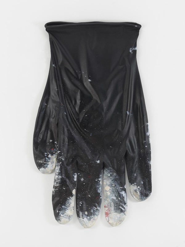 A glossy-black latex glove has white paint splatters on the finger tips.